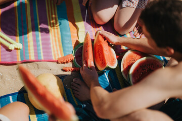 Young friends gather on a sandy beach to enjoy fresh watermelon slices together, celebrating summer...