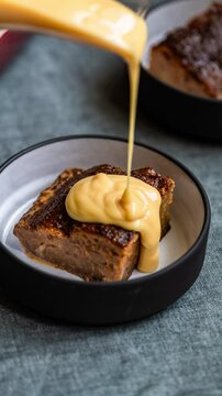 Custard being poured a slice of Malva pudding. A traditional South African baked dessert.