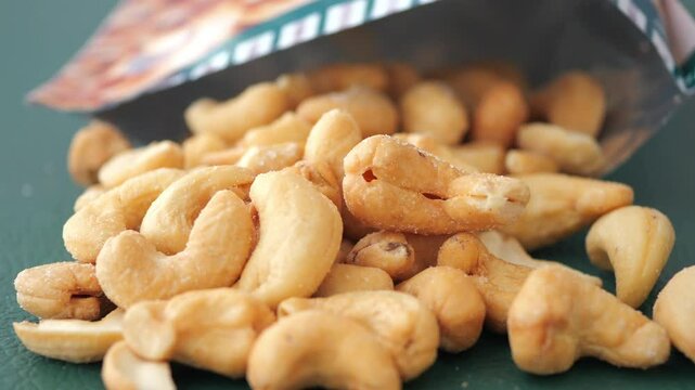 Cashews spilling out from a snack package on green surface