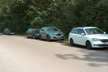 Vehicles parked along a quiet road surrounded by trees on a sunny afternoon