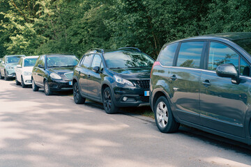 Cars parked along a tree-lined street, showcasing a mix of vehicle types and colors during a sunny day