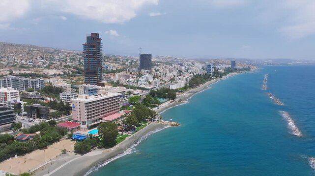 Smooth aerial sweep of Limassol, Cyprus, showing the coastline, wave breakers, modern high rises, smaller buildings, and an under construction skyscraper.