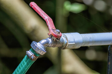 A weathered red outdoor faucet in a rustic installation to a piece of pvc pipe with a green hose, in a farm in the eastern Andean mountains of central Colombia near the Iguaque natural reserve.