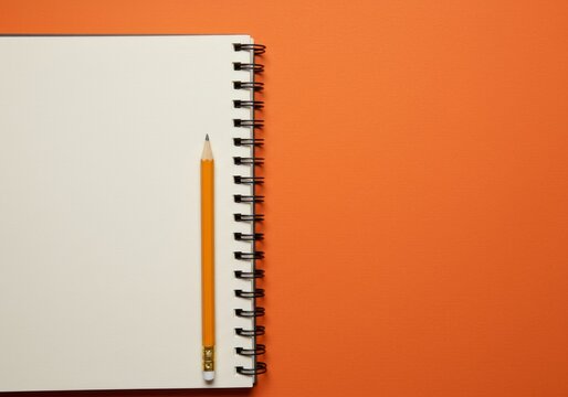 Spiral notebook with blank pages and pencil on orange background