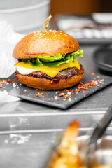 A close-up of a gourmet burger with a sesame seed bun, fresh lettuce, melted cheese, and a juicy beef patty, garnished with spices on a dark slate plate