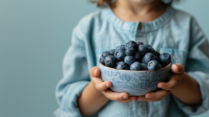 A cute child proudly holding a bowl filled with fresh blueberries, capturing innocence and joy associated with natural fruits and healthy eating habits.