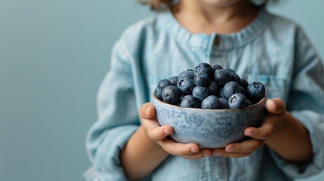 A cute child proudly holding a bowl filled with fresh blueberries, capturing innocence and joy associated with natural fruits and healthy eating habits.