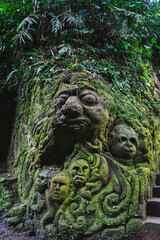 A moss-covered stone sculpture in a tropical jungle in Bali, Indonesia