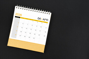 Top view of April 2026 desk calendar on black leather background.