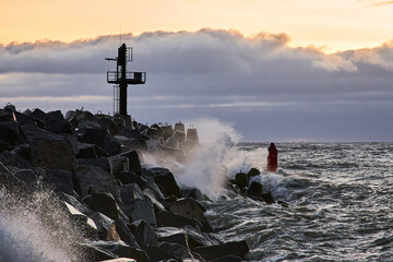The sea surf breaks on a stone breakwater against the background of sunset
