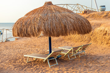 Straw beach umbrella with sun loungers on the shore of the Red Sea