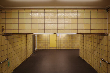 An empty, utilitarian passageway with distinctive yellow tiled walls and fluorescent lighting, characteristic of a historic Berlin U-Bahn or S-Bahn