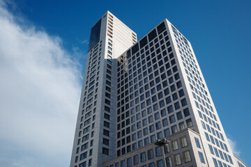 Fototapeta premium Low angle exterior view of the contemporary white curved skyscraper and modern commercial buildings against a blue sky in Berlin Germany during daytime. 