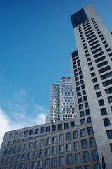 Obraz premium Low angle exterior view of the contemporary white curved skyscraper and modern commercial buildings against a blue sky in Berlin Germany during daytime. 