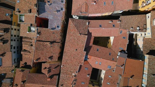 Drone flight over traditional red tile rooftops of Lazise, Italy. Aerial top-down view of historic buildings and narrow streets in warm morning light.