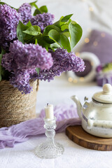 a bouquet of lilacs in a wicker basket. Romantic atmosphere on a lilac background with candles. Aluminum Teapot