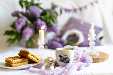 a cup with a hot drink. Breakfast with waffles and cakes, a bouquet of lilacs in a wicker basket