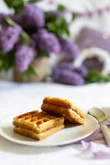 a cup with a hot drink. Breakfast with waffles and cakes, a bouquet of lilacs in a wicker basket