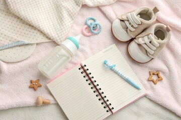 Flatlay of parenting essentials: baby bottle, pacifier, journal, tiny shoes, and toys on soft pastel blanket. Clean and gentle feel.