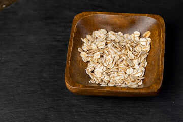 oat flakes poured into a square-shaped one wooden bowl, oatmeal for quick cooking of porridge ,...