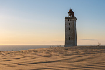 A majestic lighthouse rises from the sandy dunes, overlooking the tranquil waters of the North Sea, Rubjerg Knude, Denmark