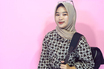 Portrait of a muslim schoolgirl carrying books in her hands and wearing a black backpack on an isolated background