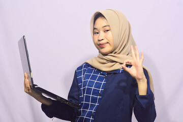 Portrait of a smart-faced Muslim female student wearing glasses, holding her laptop