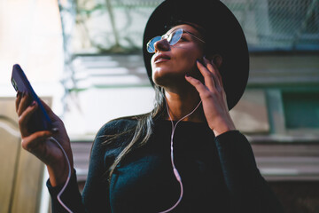 Stylish brunette woman listens to music with smartphone and earphones, eyes closed, enjoying sound and moment, embodying personal space within digital connection.