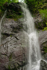 Obraz premium A magnificent waterfall flows over steep, rocky terrain, creating a serene atmosphere with its soothing sound. Vibrant greenery frames the natural wonder, highlighting the beauty of Batumi, Adjara.