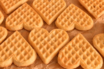 Belgian waffles in heart shape on baking paper. Homemade and soft, ready to serve or style.
