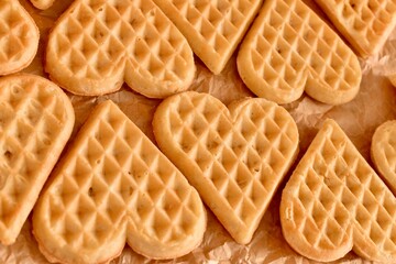 Golden heart-shaped waffles aligned on parchment paper. Warm tones, soft texture, overhead food composition.

