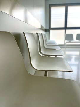 Row of empty chairs in a hospital waiting room. Clean, sterile environment with minimal furniture and white walls.