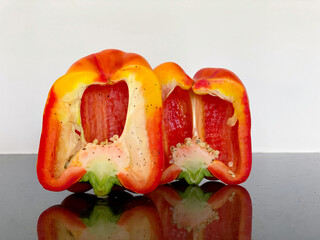 A vibrant red bell pepper is cut in half, revealing its juicy flesh and seeds. The smooth, shiny surface reflects the colorful vegetable, emphasizing its freshness and texture.