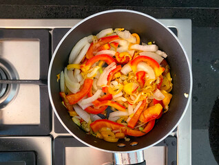 A skillet on a stovetop holds a vibrant stir-fry with sliced bell peppers, mushrooms, onions, and assorted vegetables cooking.