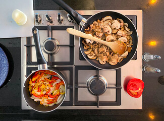 Fresh mushrooms are sliced and saut&eacute;ed in a skillet on a sleek stovetop. A wooden spoon is used to stir the mushrooms as they cook, highlighting the culinary process.