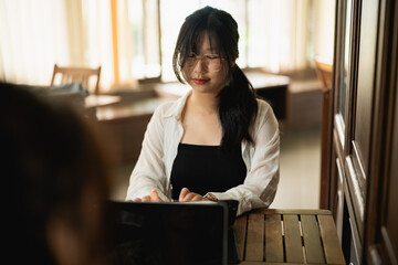Young woman with glasses working on laptop in cozy cafe setting, focused on tasks with warm natural...