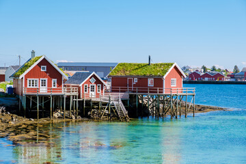 Explore the vibrant red fishing huts on stilts by the serene waters of Norway coastal landscape