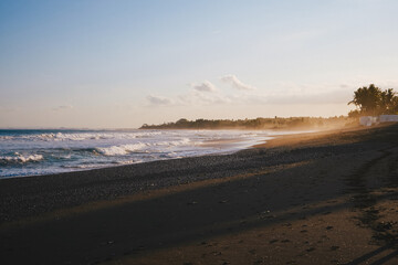 Scenic view of a tropical Keramas beach at sunset with gentle waves, golden light, and dark sand, creating a peaceful and serene coastal atmosphere in Bali, Indonesia