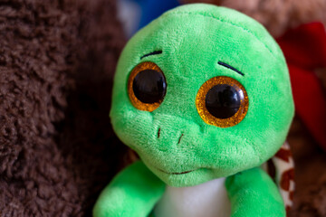 Cute plush turtle with big eyes sitting among soft toys