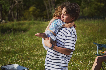 Young Boy Holding a Sibling Amidst a Scenic Outdoor Picnic Setting