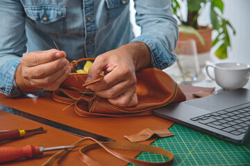 Leather craftsman carefully hand-stitching a stylish bag in his workshop, demonstrating traditional...