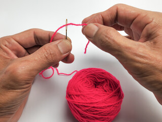 Person threading a needle with bright pink yarn ready to sew