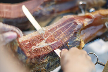 Close-up of traditional Spanish jamón being hand-sliced with a sharp knife. Thin slices of cured ham with rich marbling. Authentic gourmet delicacy in the making.