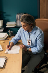 Middle aged Caucasian woman with gray hair wearing blue shirt and social worker badge sitting at...