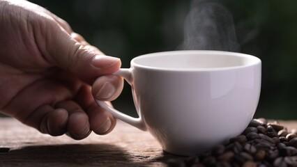 Hand holding a Steaming recycled paper coffee cup with americano coffee green environment close-up viewpoint