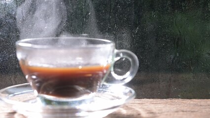 Steaming mug of Americano coffee with raindrops on window glass background, cozy beverage concept, close-up view.