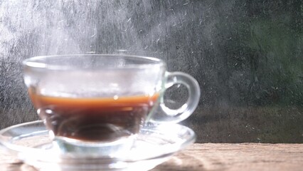 Steaming mug of Americano coffee with raindrops on window glass background, cozy beverage concept, close-up view.