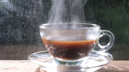 Steaming mug of Americano coffee with raindrops on window glass background, cozy beverage concept, close-up view.
