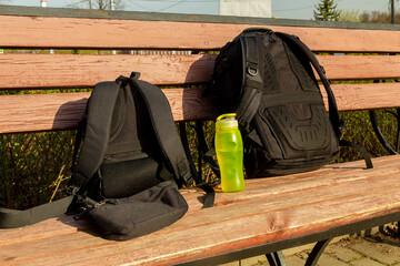 Two photo backpacks and a water bottle on a bench with a backrest
