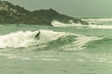 Surfer riding wave on cloudy morning near rocky coastline